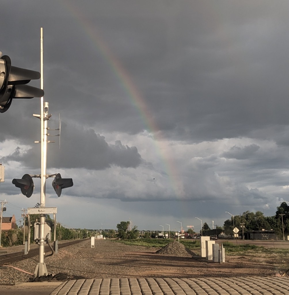 Train tracks, cloudy sky with a rainbow.