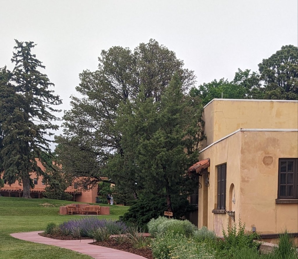Fountain Valley School pathway onto campus from the parking lot behind the Hacienda building. Adobe buildings, tall evergreen trees, xeriscape gardens.